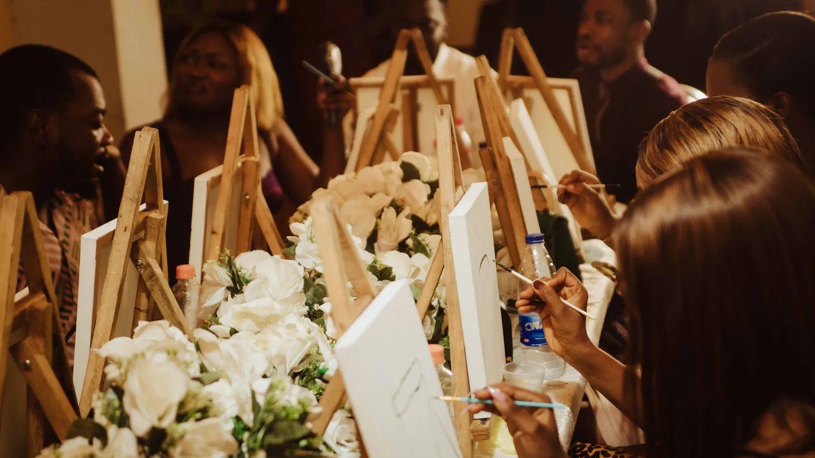 Photo: McFollis on Pexels A group of friends painting at easels around a long table set with white flowers
